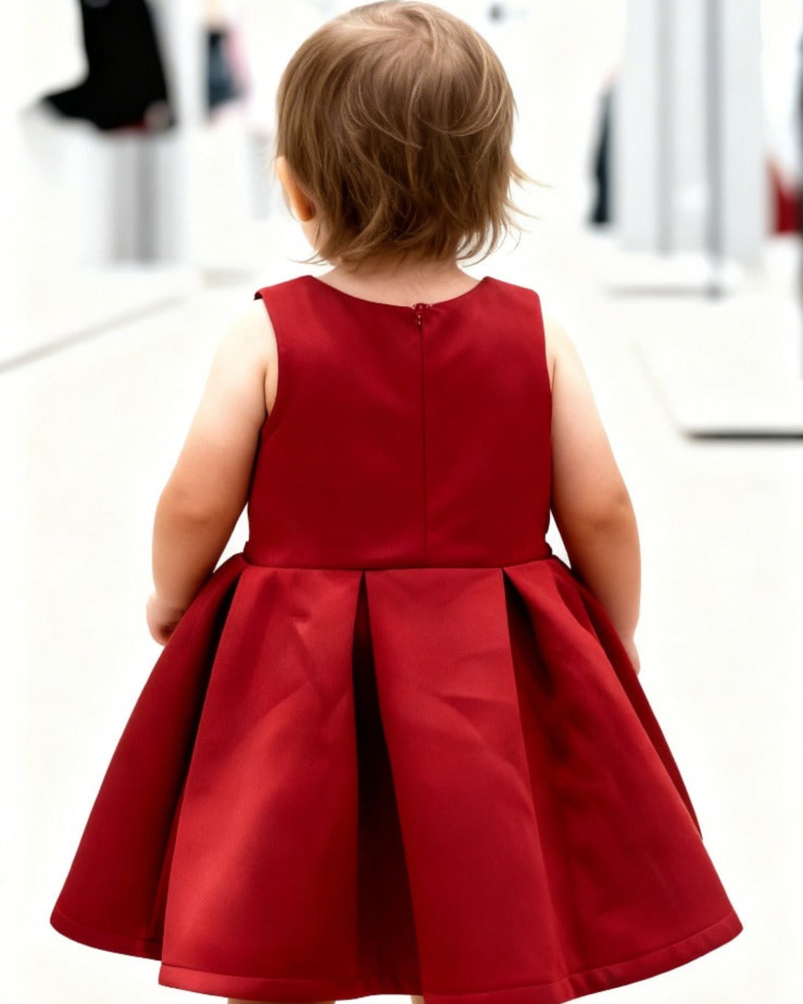 Child wearing a red dress standing in a white room with mirrors.