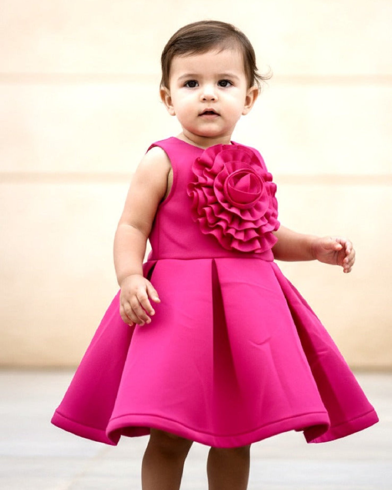Child wearing a bright pink dress with floral details against a neutral background
