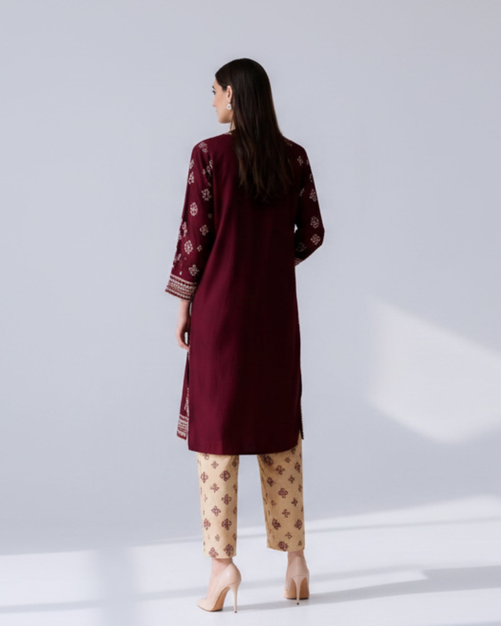 Woman wearing a burgundy embroidered kurta with beige pants in a minimalistic setting.