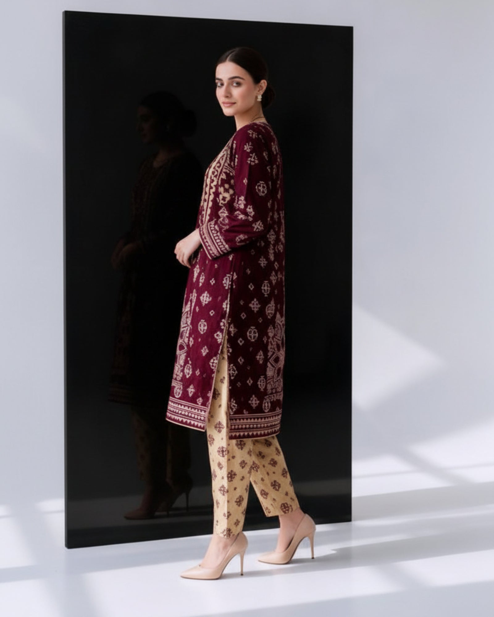 Woman wearing a maroon embroidered outfit with beige pants in a studio setting