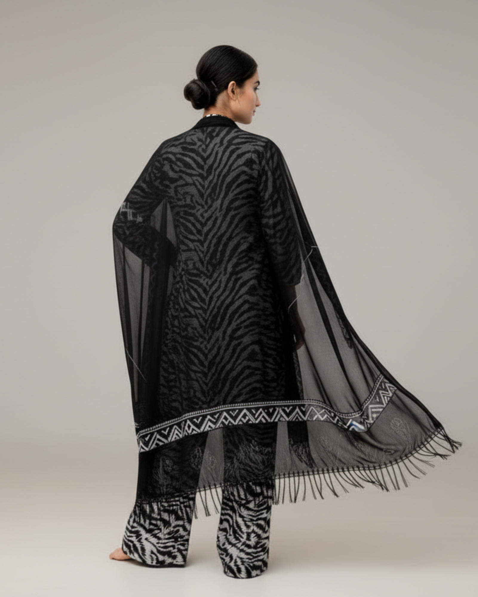 Woman wearing a black patterned outfit with a sheer dupatta on a white background