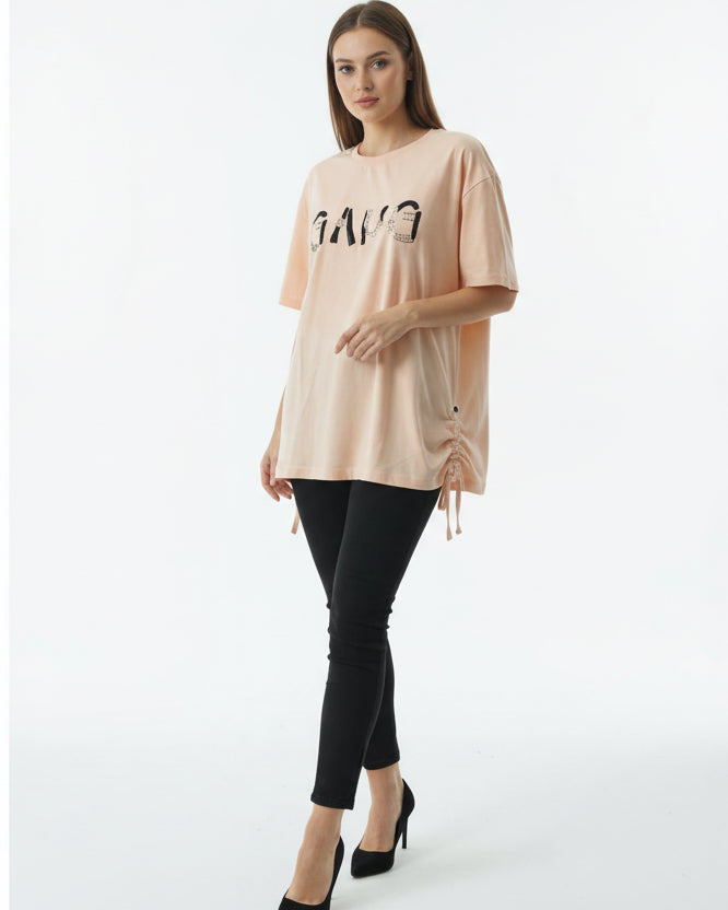 A woman stands against a white background wearing the Softform Classic Tee, black leggings, and black heels. She holds the side of her shirt, highlighting this soft, breathable daily wear with a neutral expression.