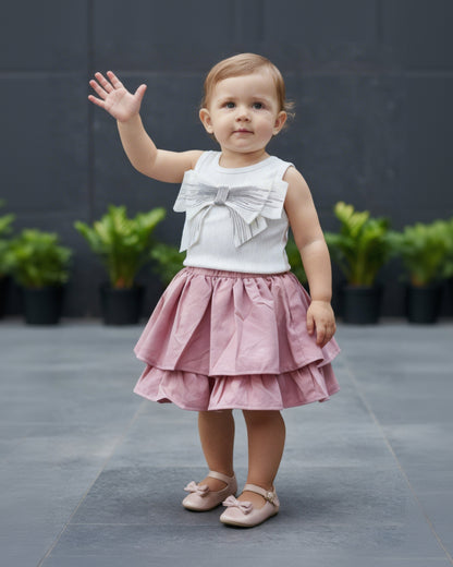 Child wearing a white top with a bow and a pink skirt, standing outdoors.