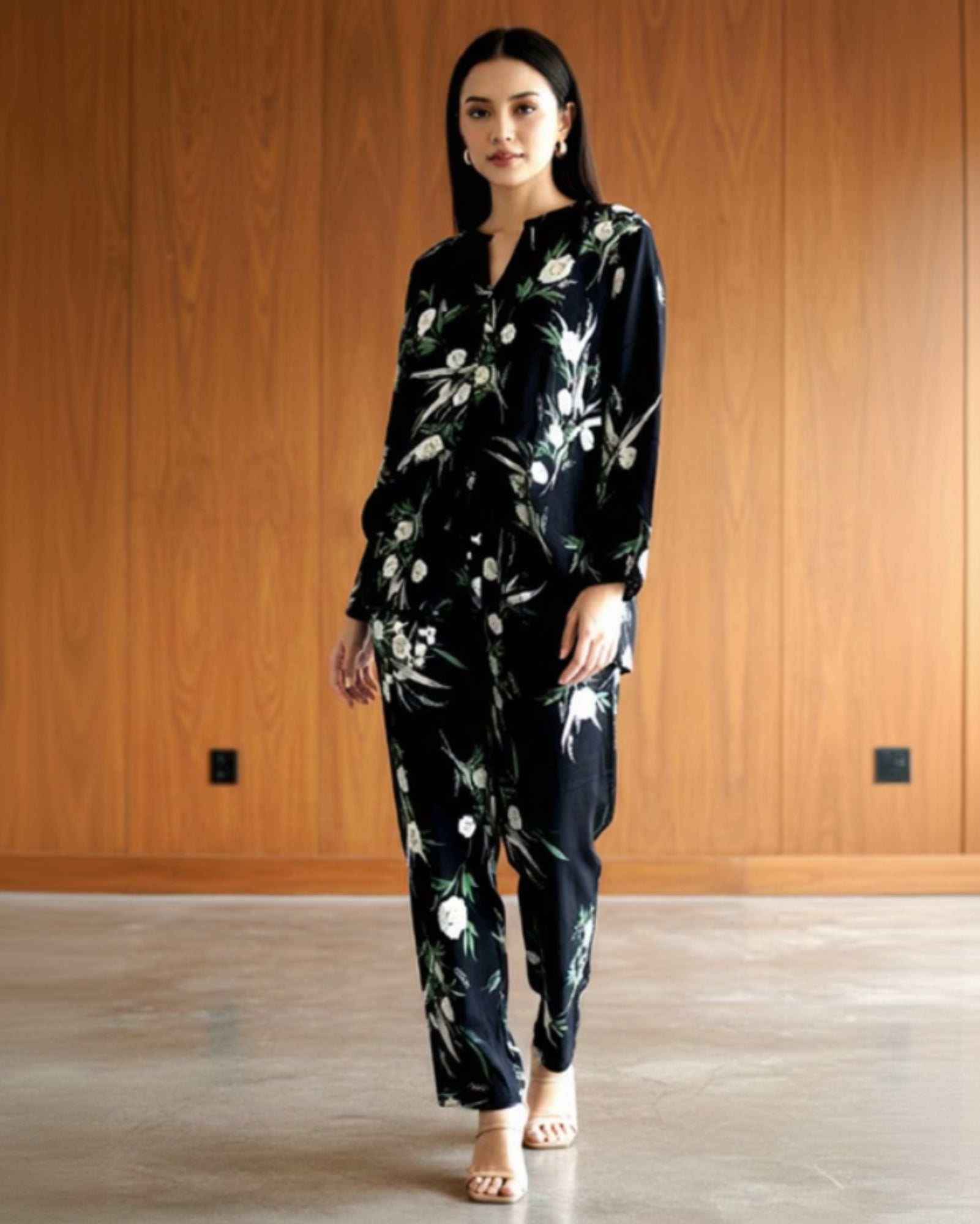 A woman stands indoors against a wood-paneled wall and concrete floor, wearing the Modern Muse Co-Ord and light-colored heeled sandals for a contemporary, floral-inspired look.