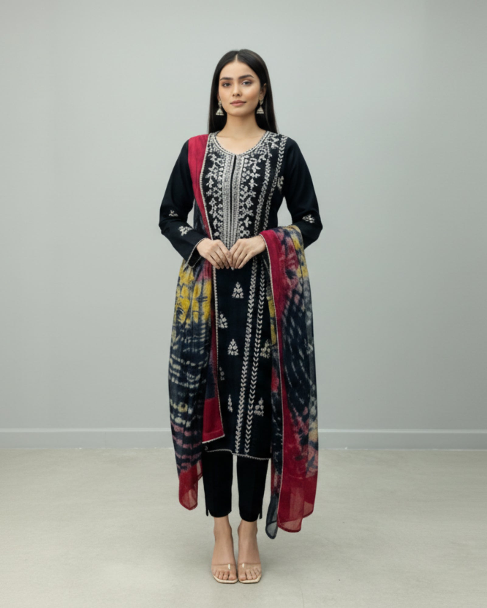 Woman wearing a black embroidered outfit with a red dupatta against a white background