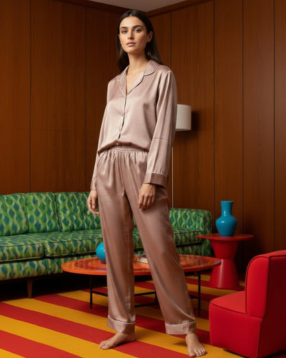 Woman in a beige satin pajama set standing in a room with colorful decor.