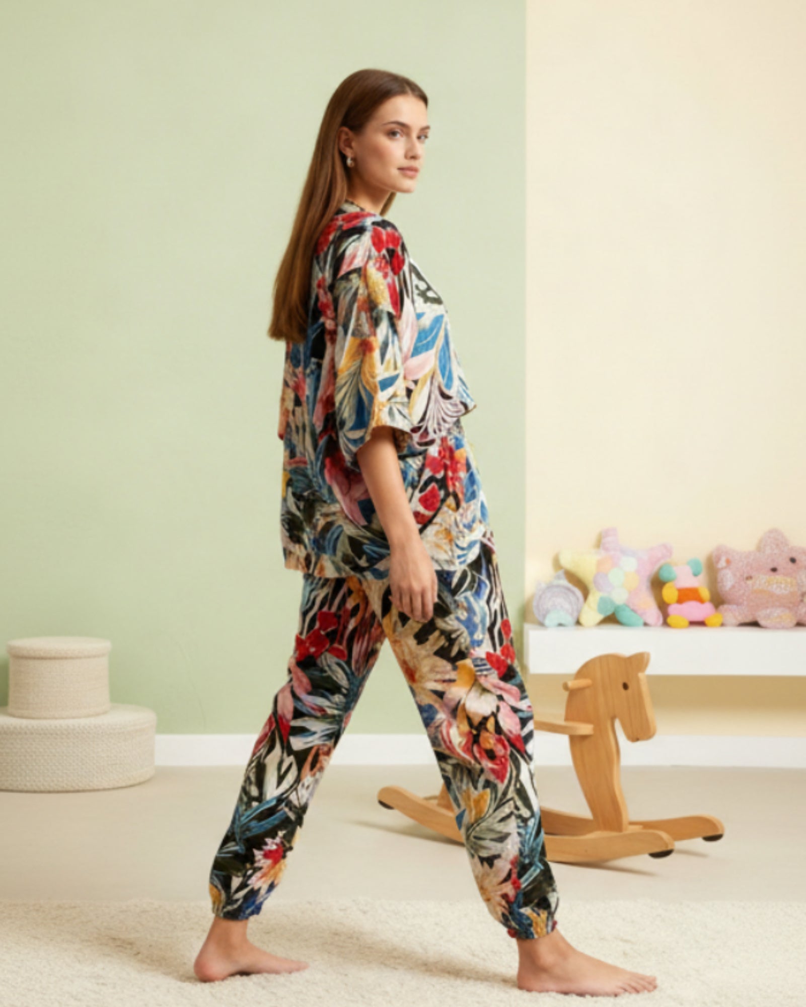 Woman wearing a colorful floral pajama set in a room with a green wall and wooden horse toy.