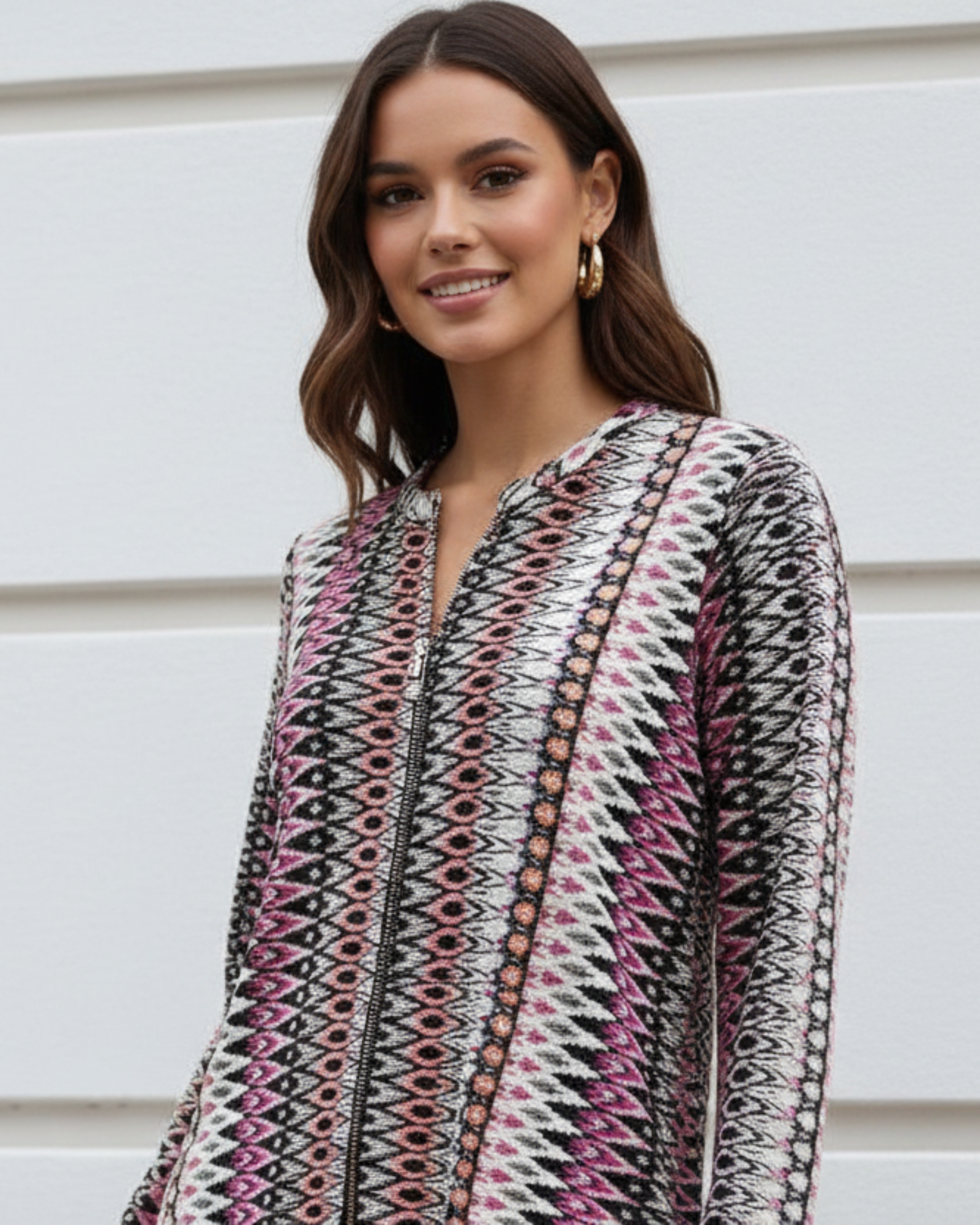 Woman wearing a patterned outfit standing against a light-colored wall.