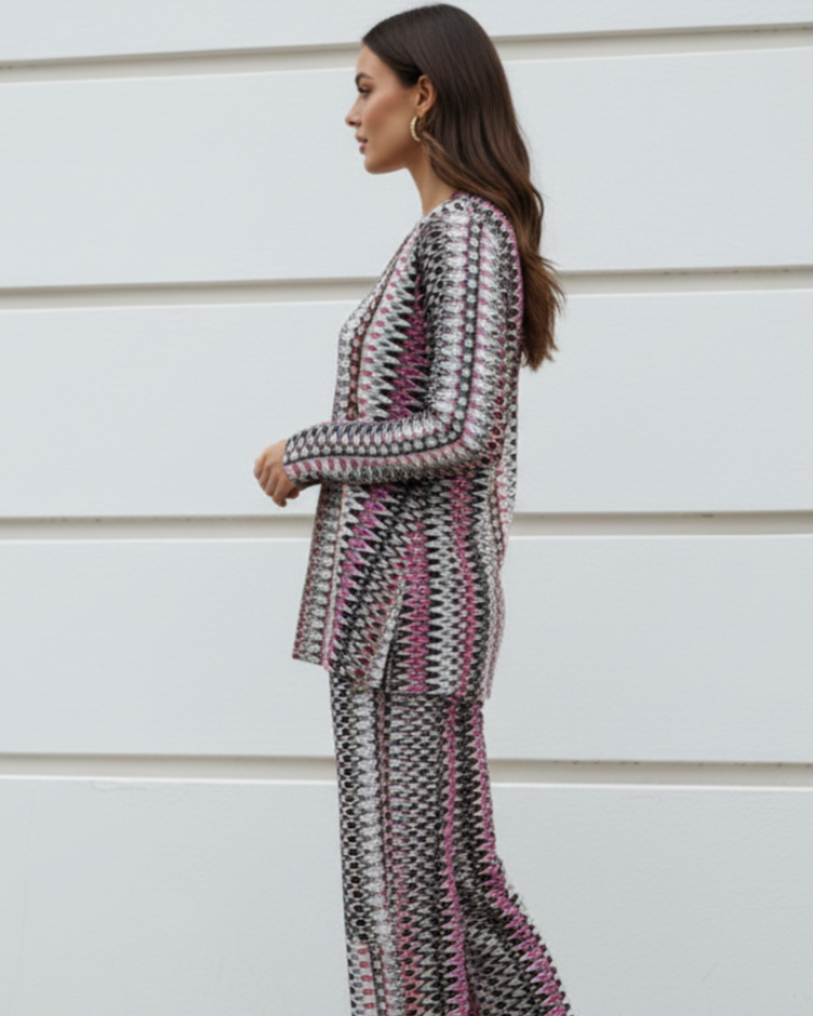 Woman wearing a patterned outfit standing against a light-colored wall.