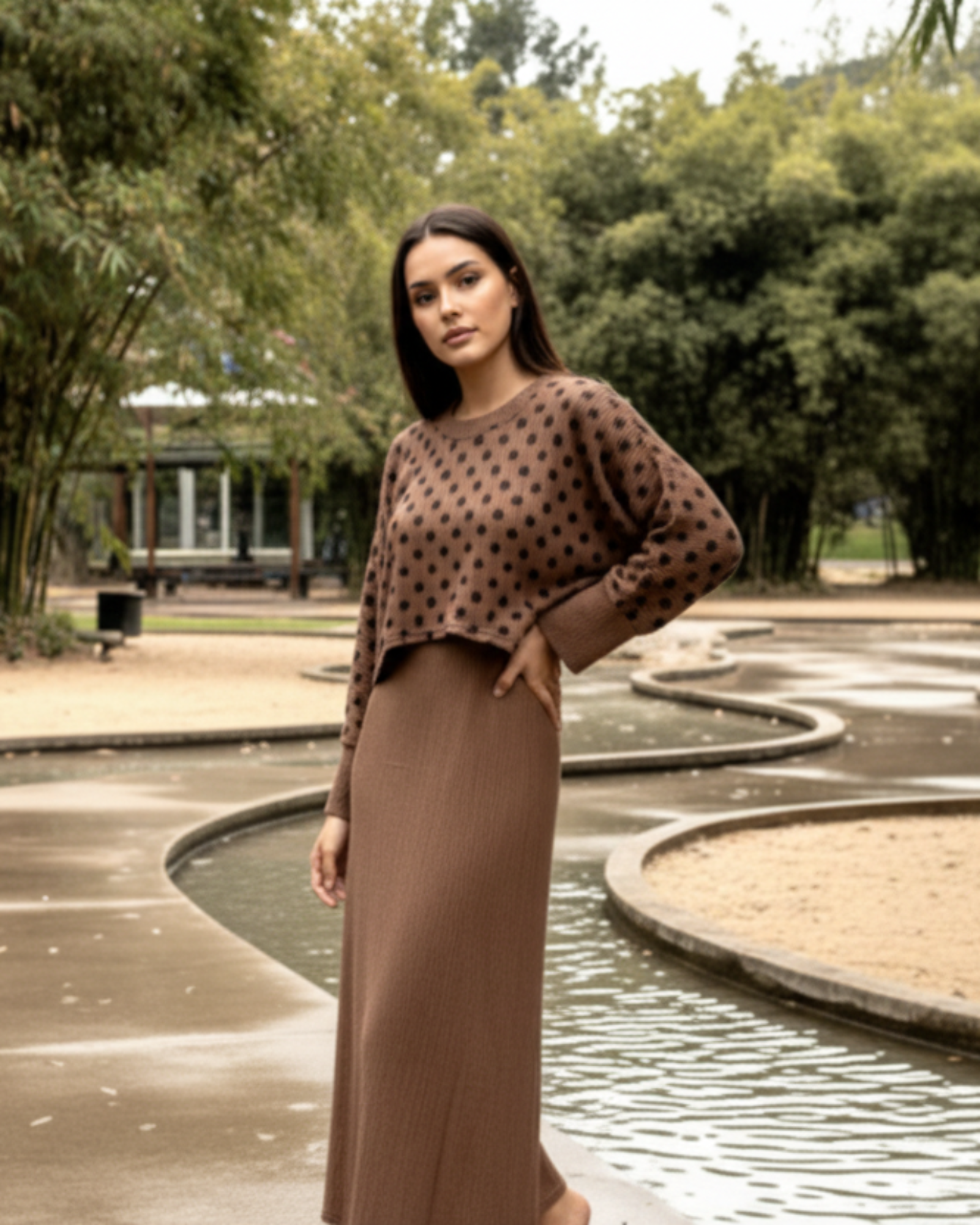 Woman wearing a brown polka dot top and long skirt standing in a park.
