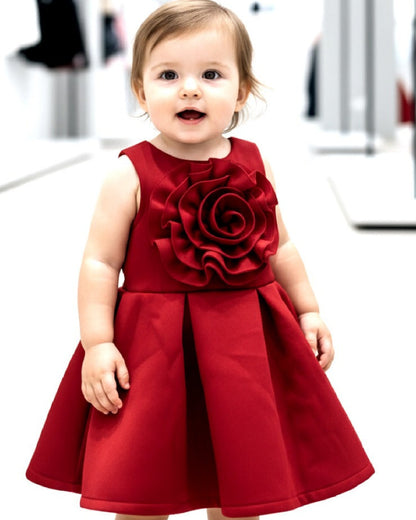 Child wearing a red dress with a large flower design in a blurred indoor setting