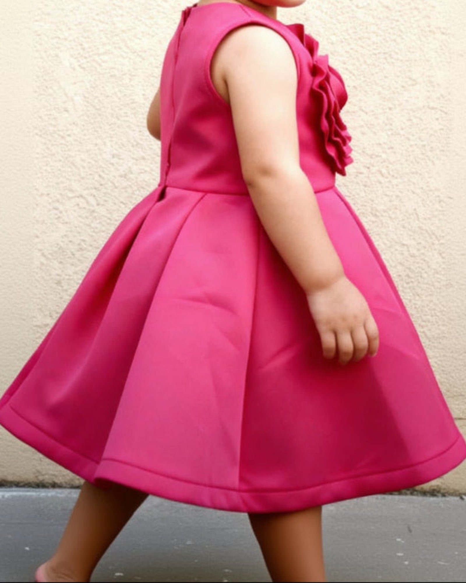 Child wearing a bright pink dress with a flower detail on a plain background