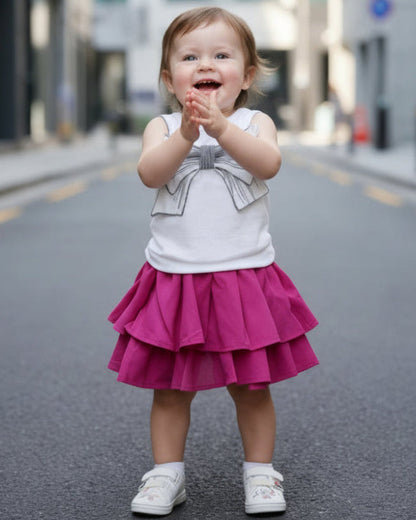 Child in a white top with a bow and pink skirt waving on a city street.