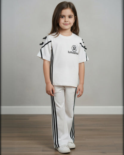 Young girl wearing a white outfit with black accents and a visible brand logo on a plain background