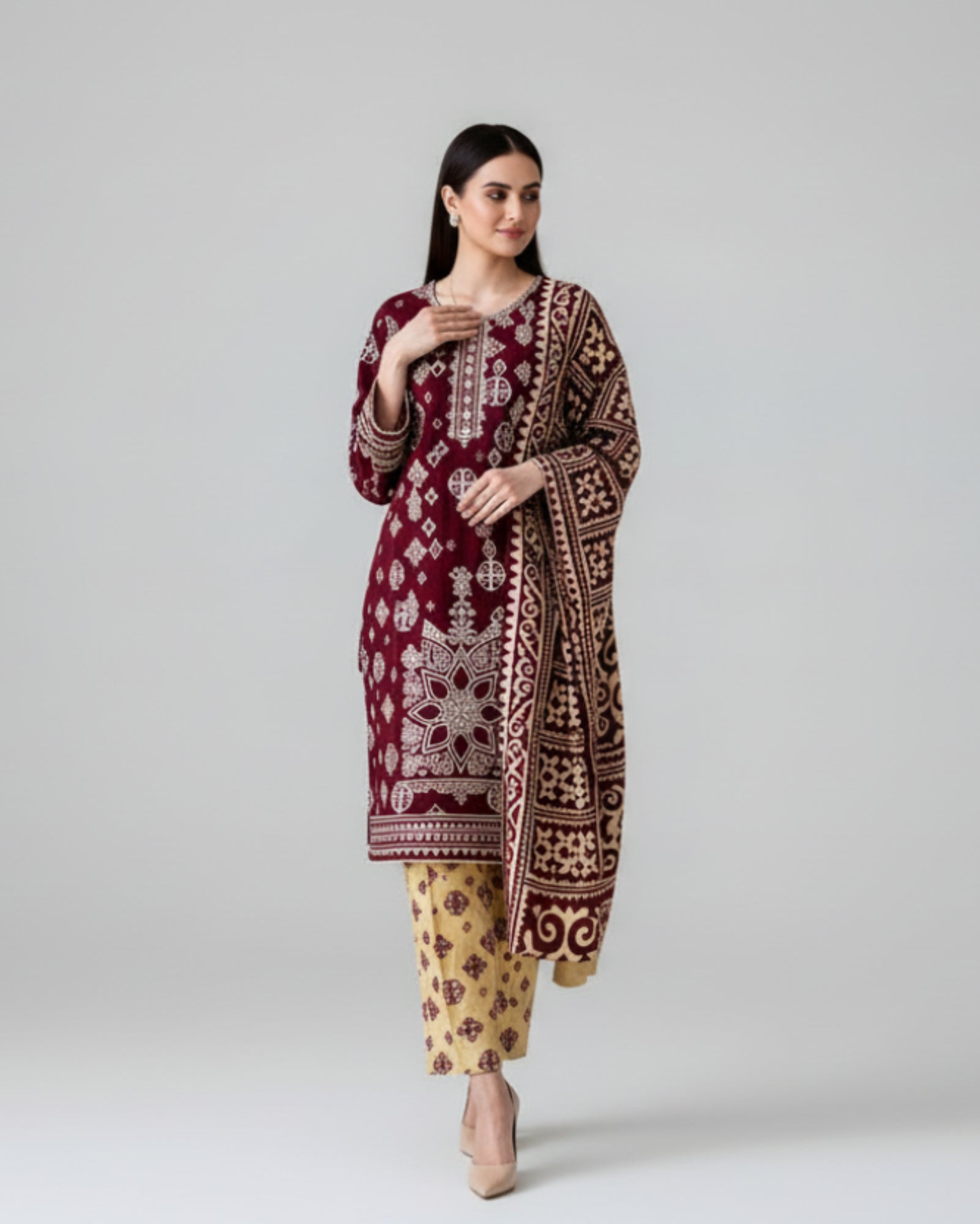 Woman wearing a maroon embroidered traditional outfit with yellow pants, standing against a black background.
