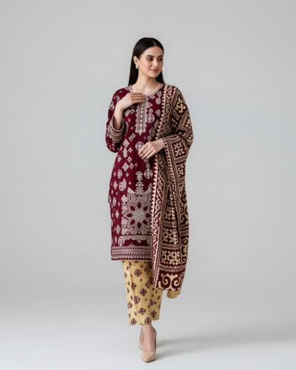 Woman wearing a maroon embroidered traditional outfit with yellow pants, standing against a black background.