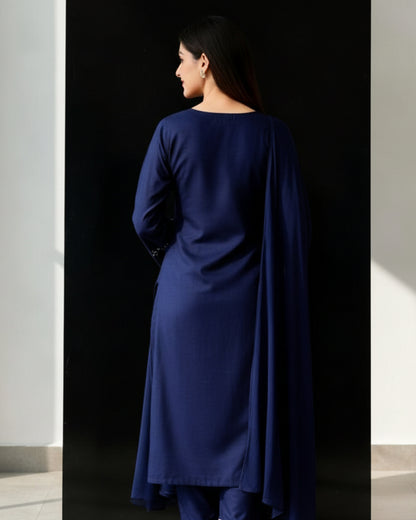 Woman wearing a dark blue embroidered traditional outfit in a minimalistic setting