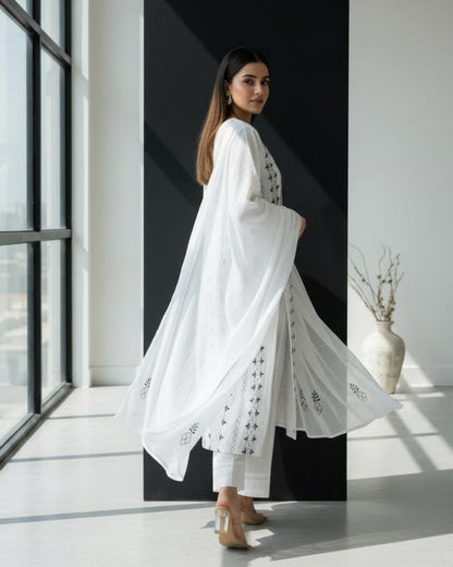 Woman in a white outfit standing in a modern interior setting with large windows.
