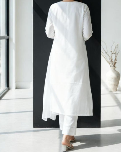 Person wearing a white dress standing in a room with large windows and minimal decor.