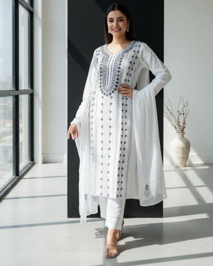 Woman in a white embroidered kurta standing in a modern room with large windows.